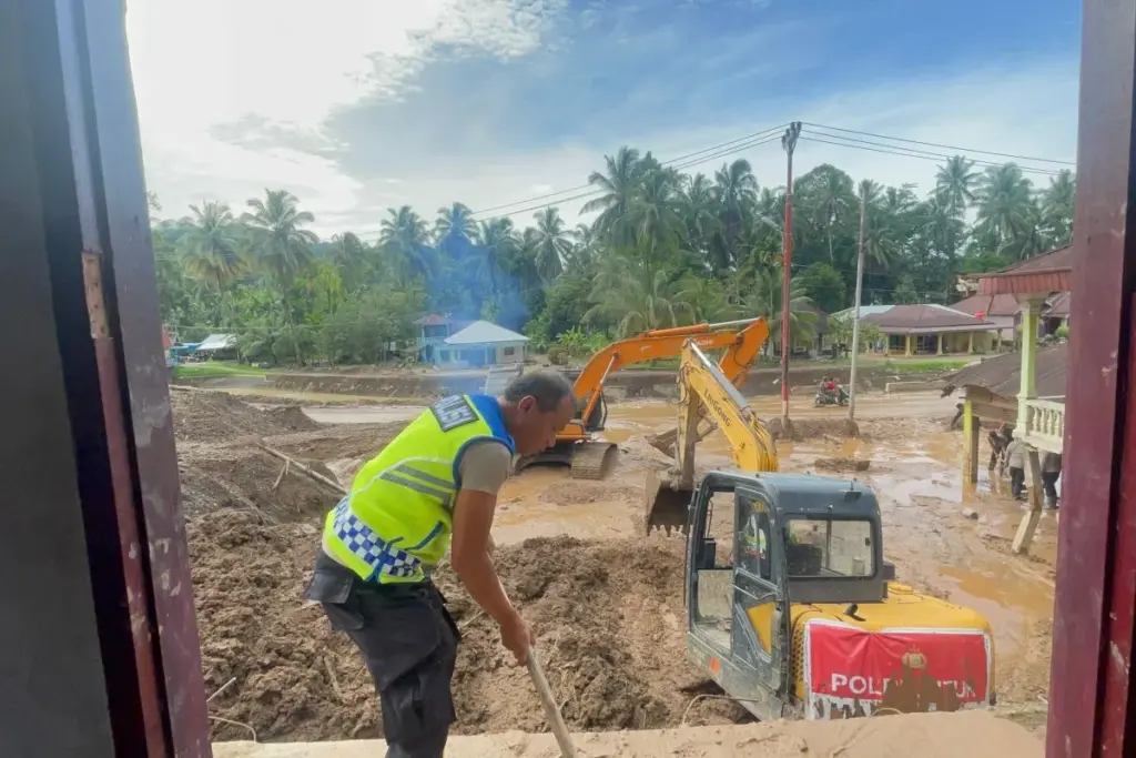 Polri Kerahkan 86 Alat Berat Percepat Pemulihan Bencana di Sumatra Seorang personel kepolisian membantu membersihkan material lumpur di lokasi bencana di Sumatra. (Foto: Polri)